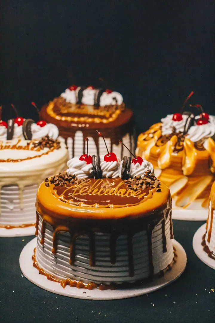 Cream cakes decorated with chocolate drips and cherries on a dark counter