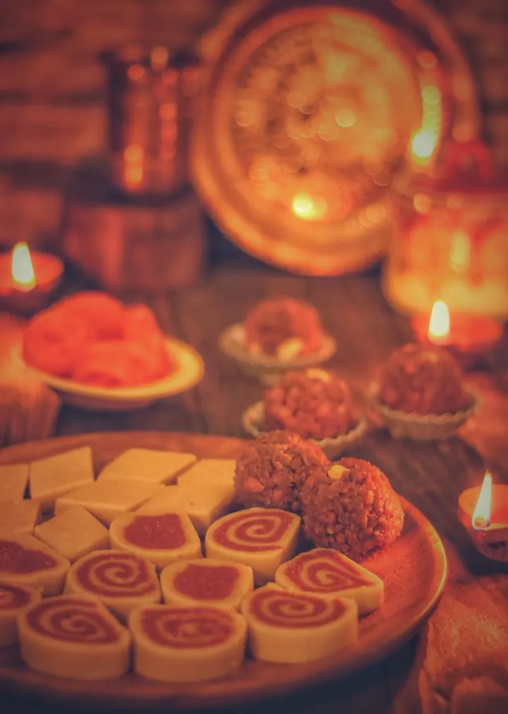 Indian sweets on plates lit by clay diyas