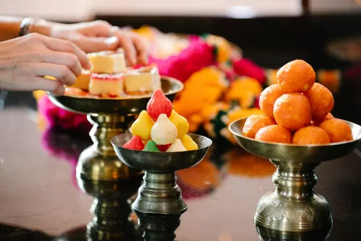 Brass stands holding ladoos, barfi and sweets beside marigold flowers